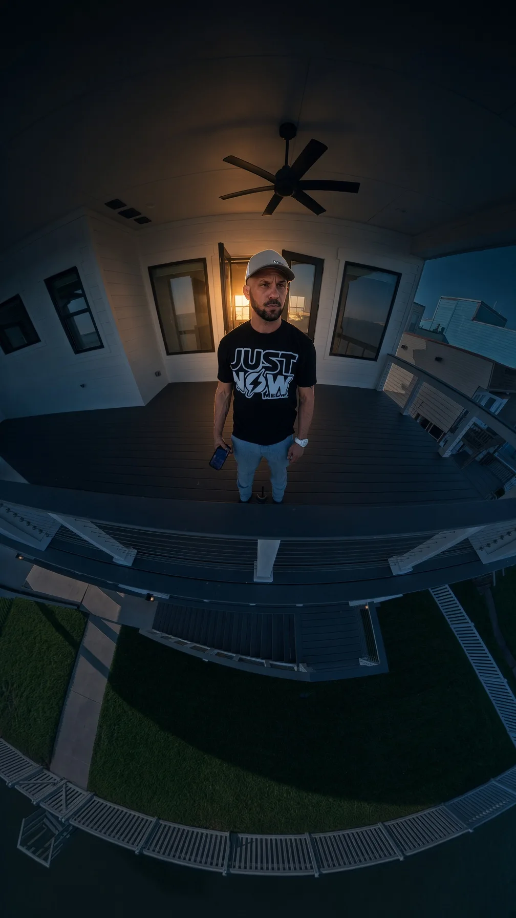 Camera operator on a waterfront balcony photographed with a wide fisheye view